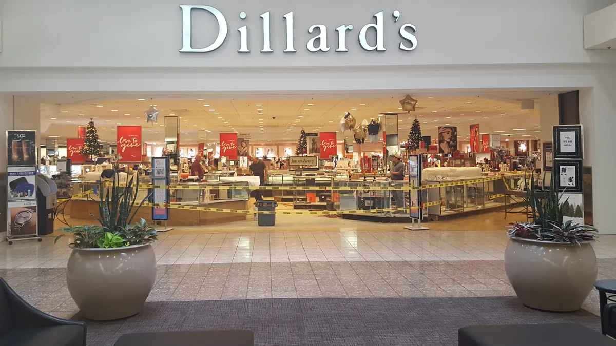 Two round beige planters on each side of a mall entrance to a Dillard's store.