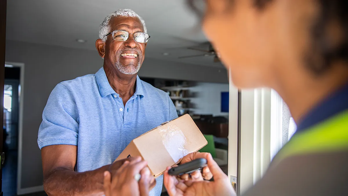 An old person smiliing receiving a package from a delivery person