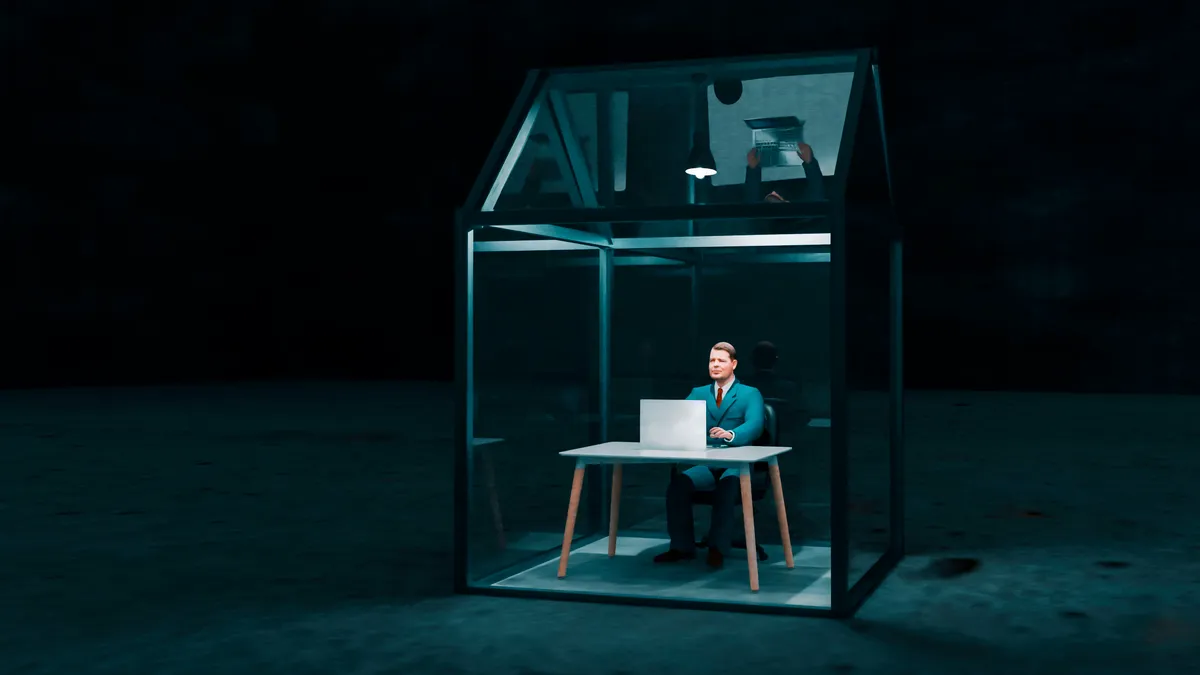 A person works on the computer in a tiny glass house, just big enough to encapsulate him