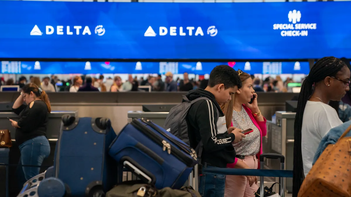 People wait in line with baggage at the Delta Airlines check-in counter.