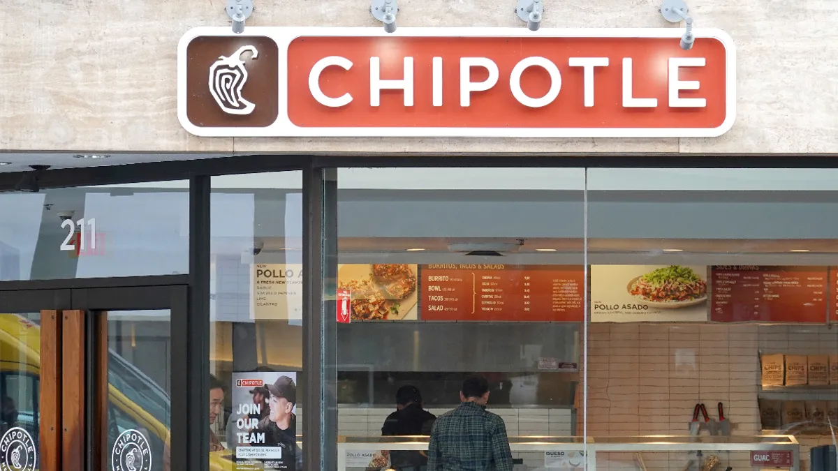 A bank of windows below a red sign that says "Chipotle." A man stands in the background inside the restaurant.