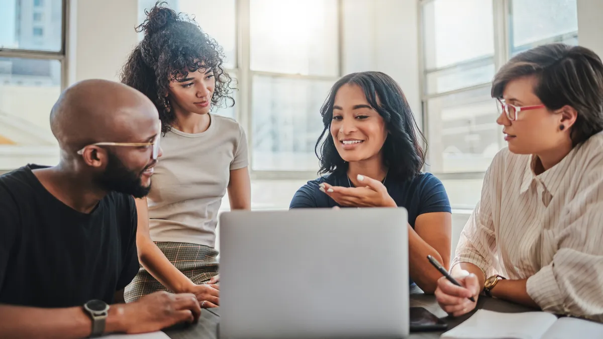 Four people have a discussion in front of a laptop.