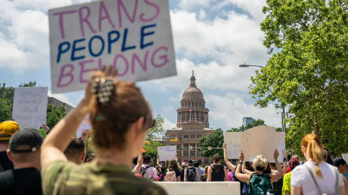 A person carries a sign that says "trans people belong" in front of the Texas capitol building.