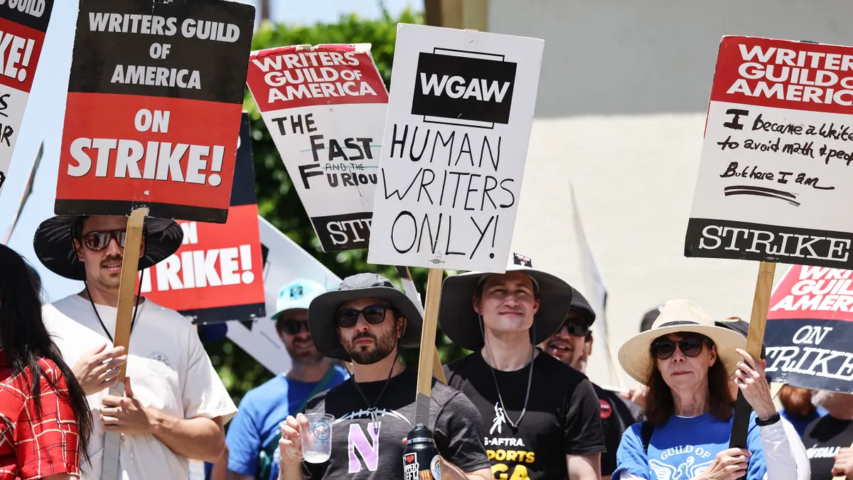 Workers are seen picketing, as one holds a sign that reads 'Human Writers Only!'
