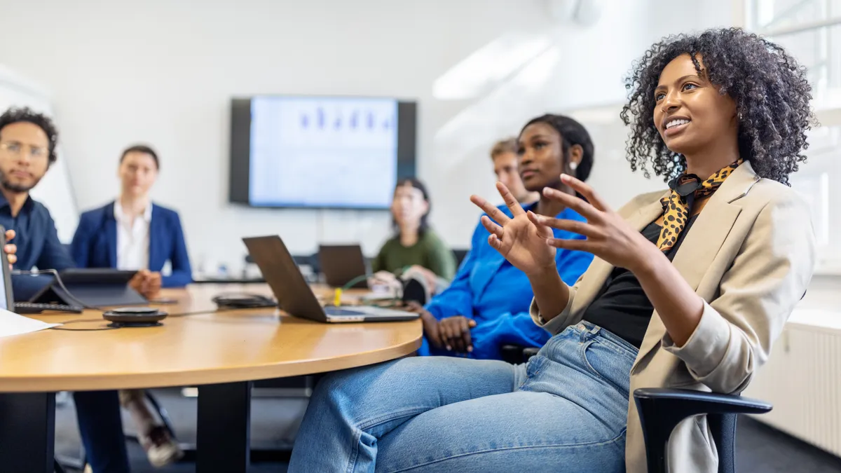 A person speaks to colleagues in a meeting room.