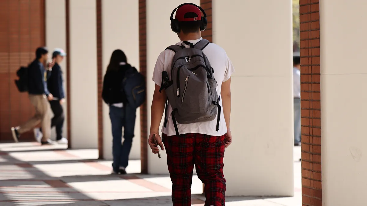 A college student walks through campus with headphones on.