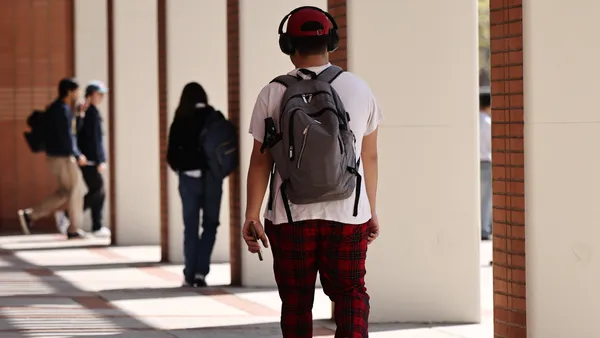 A college student walks through campus with headphones on.