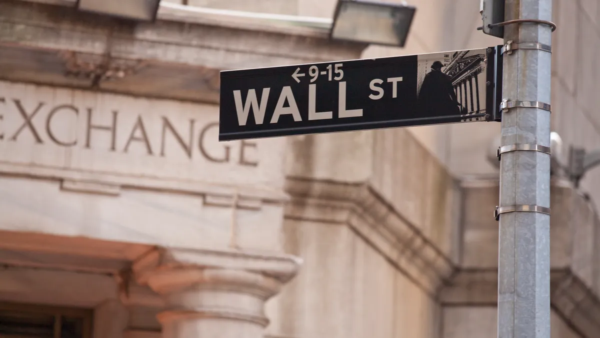 A street sign for Wall Street in front of the facade of the New York Stock Exchange.