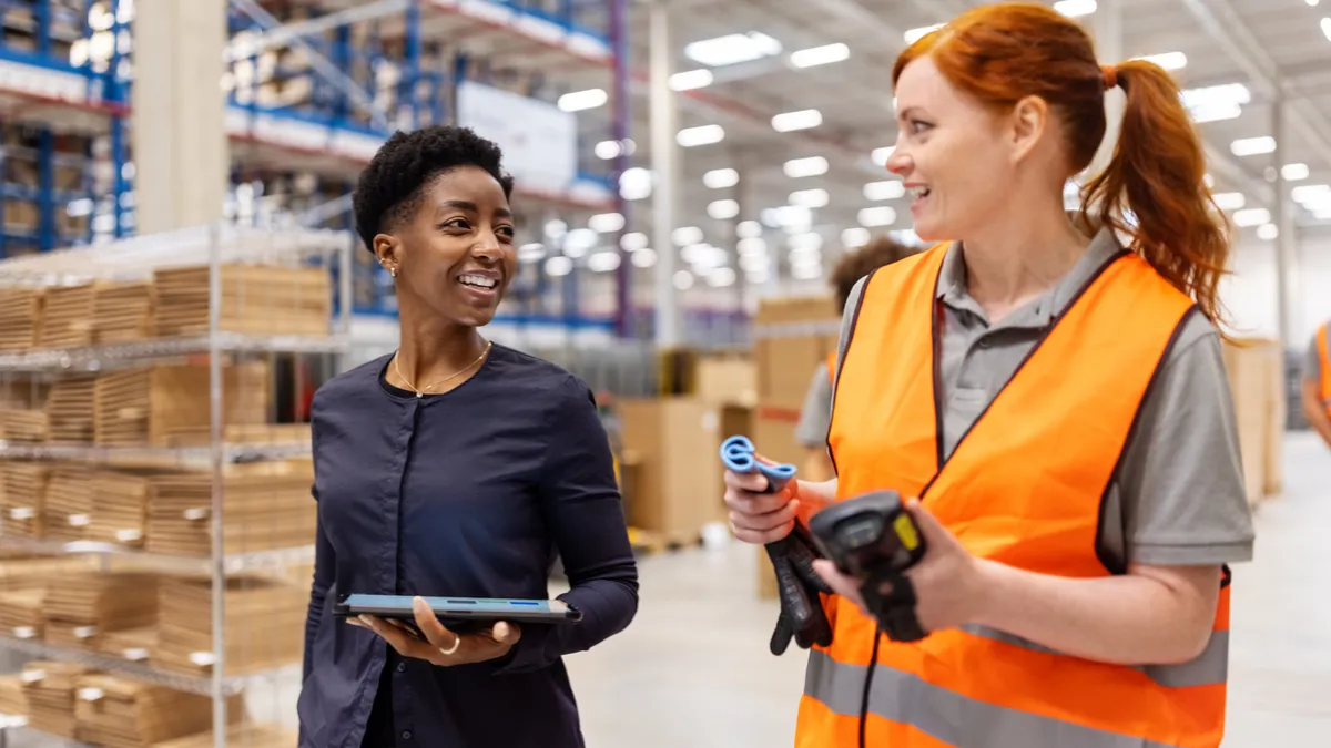 Manager holding a tablet walking and talking with a worker in a warehouse.